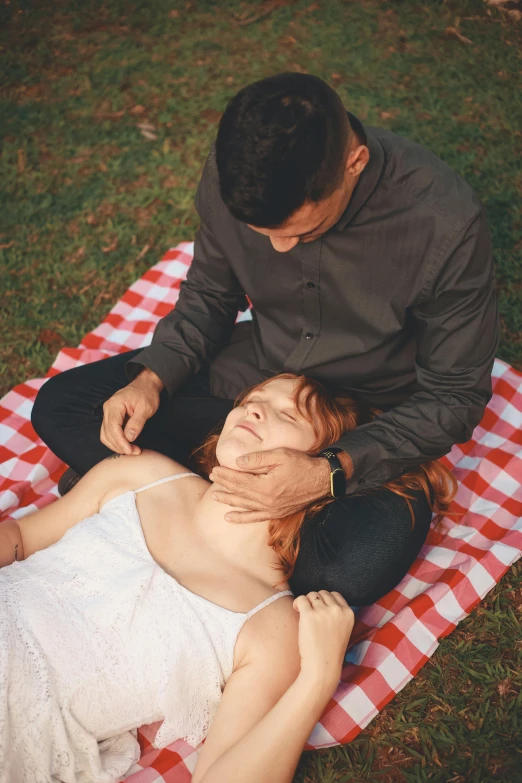 a man sitting next to a woman on top of a picnic mat