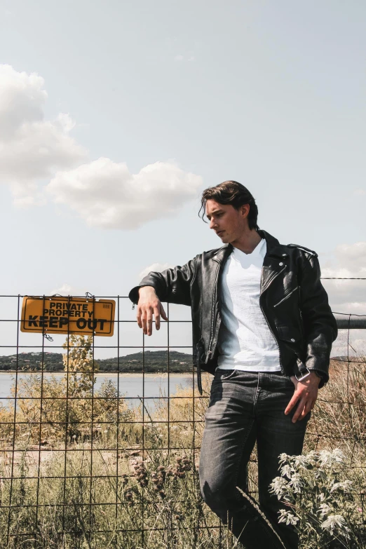 the young man is leaning against a fence pointing at a sign