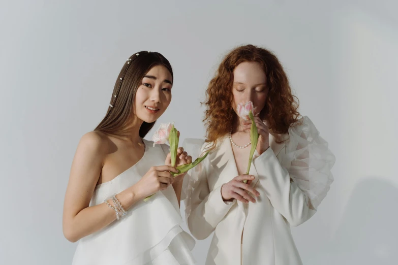 two young ladies wearing long - sleeved white outfits are holding flowers