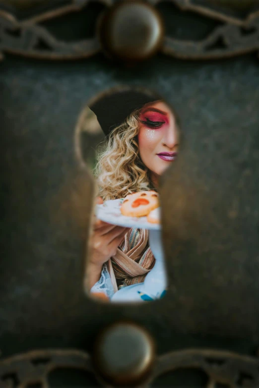 a young blond with bright makeup looking through a key hole