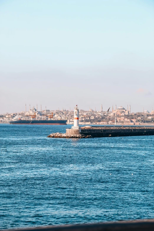 a white lighthouse stands on a ledge in the ocean