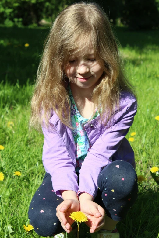 a little girl kneeling down in a grassy field, touching a flower