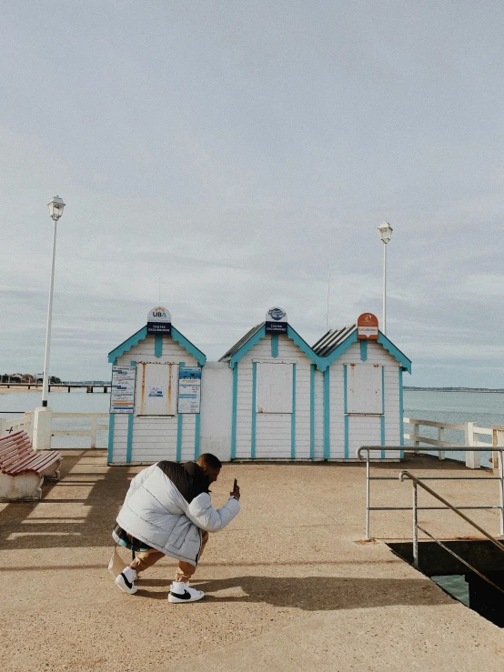 a man kneeling in front of blue and white wooden shacks on the beach