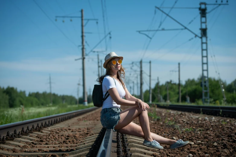 a woman wearing a hat and sunglasses sitting on a train track