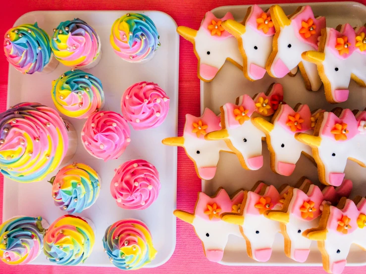 a plate of decorated sugar cookies next to a tray of cupcakes