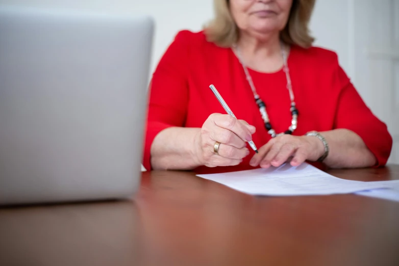 a woman is sitting at a table writing and using her laptop