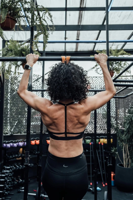 back view of a woman standing in front of the gym machines, and working on her upper arm muscles