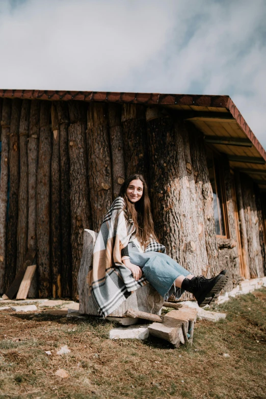 a girl sitting outside of a cabin on a chair in the grass