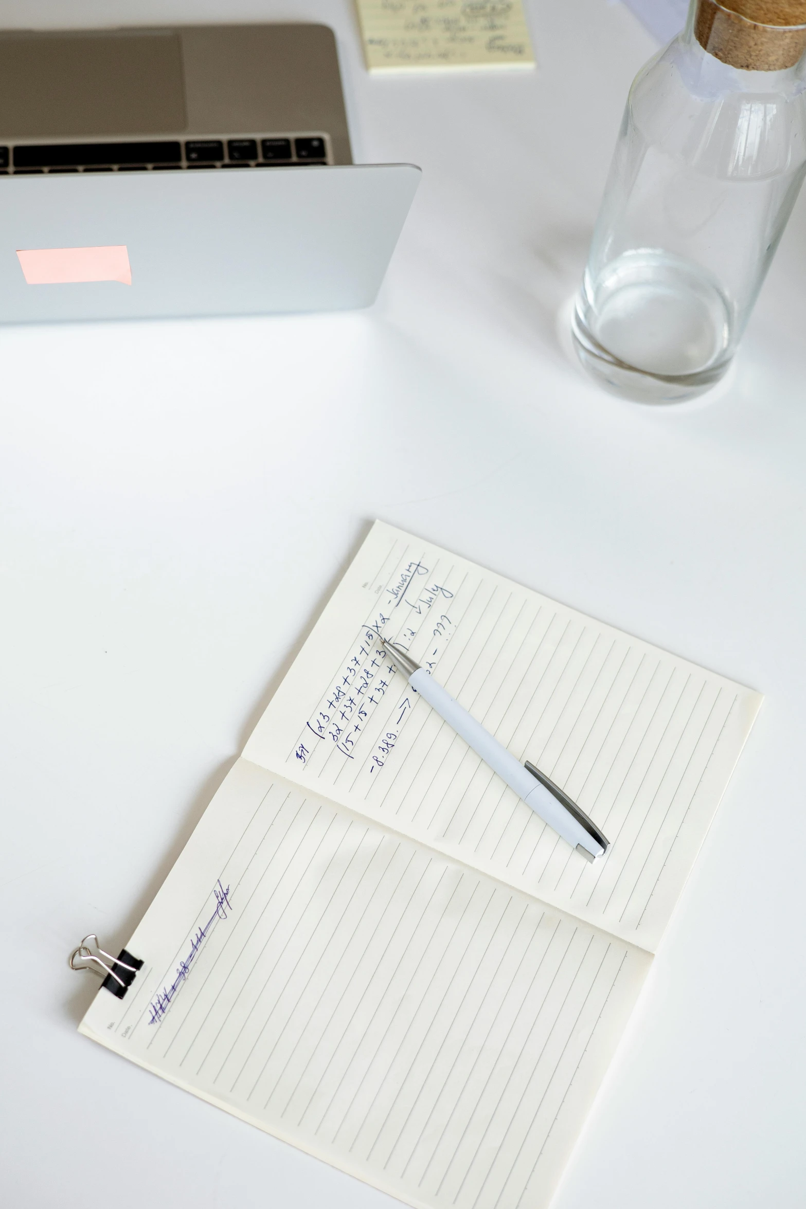 a pen and notepad with writing on a white desk