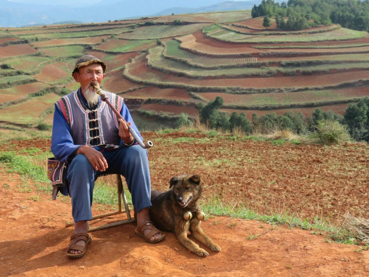 man sitting in chair with a dog on top of a hill