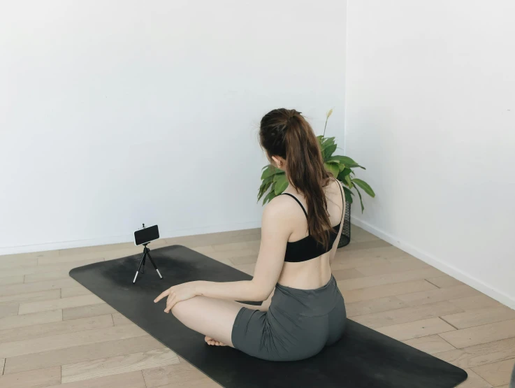 woman sits on black mat and holds up her legs