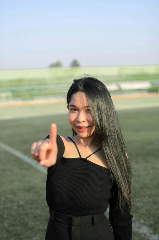 a woman giving a thumbs up sign with a soccer field in the background