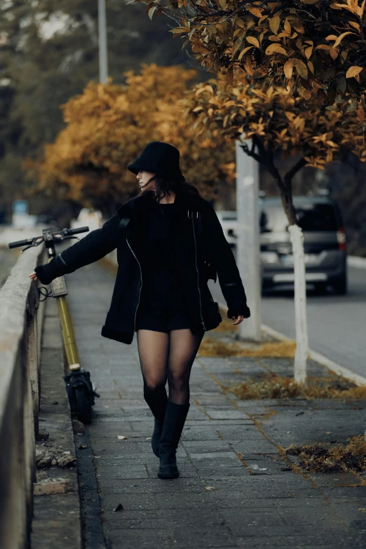 a woman with black clothing and hat is walking along the sidewalk