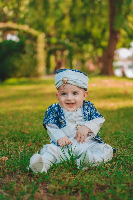 a baby wearing a blue and white outfit sits in grass