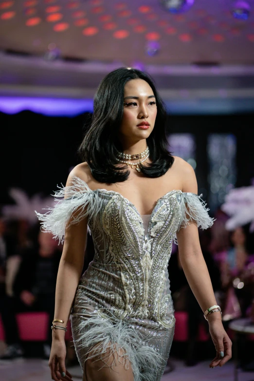 a young woman walking on the runway in a silver dress