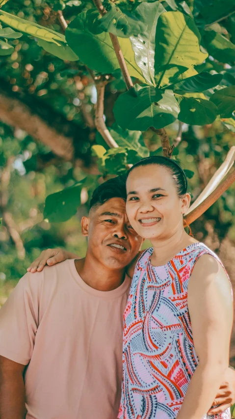 an older man and woman pose for a picture under the leaves of a tree