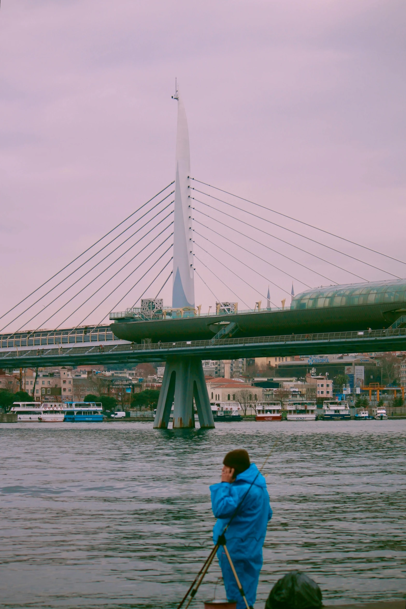 man with oars stands on the edge of the water by an enormous bridge