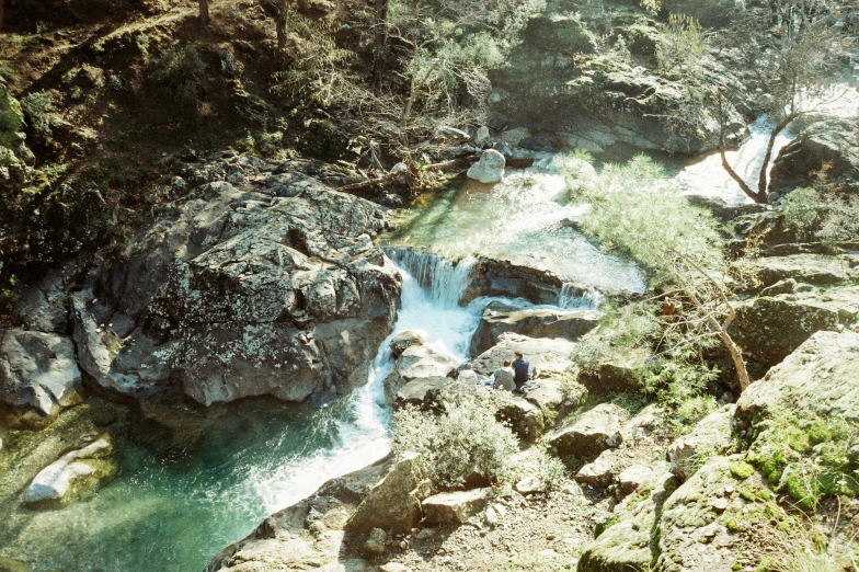 people walking along side of small waterfall near a river