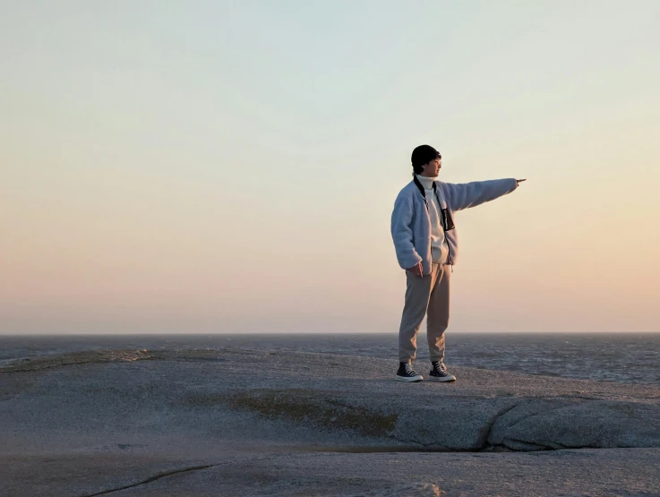 a person in a jacket and hat standing on a rock at the ocean shore