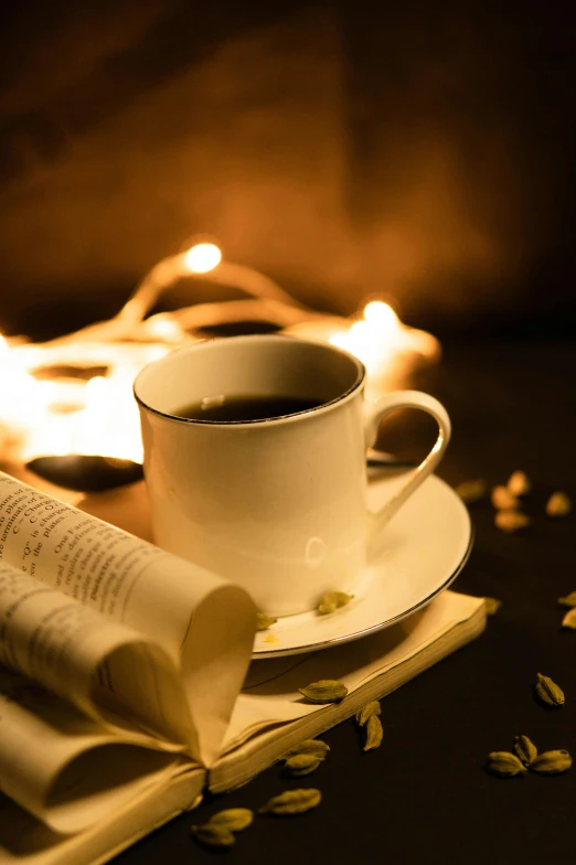 a book and cup sit on a table beside some candles