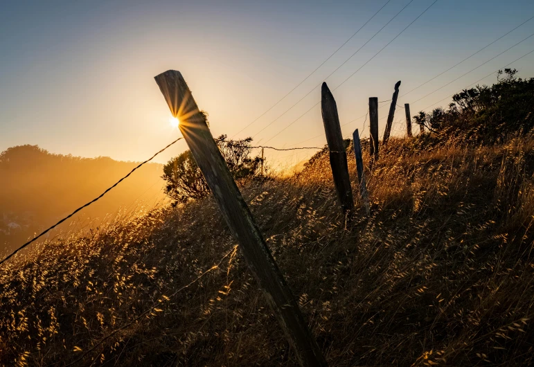 the sun shines over the mountains behind a wire fence