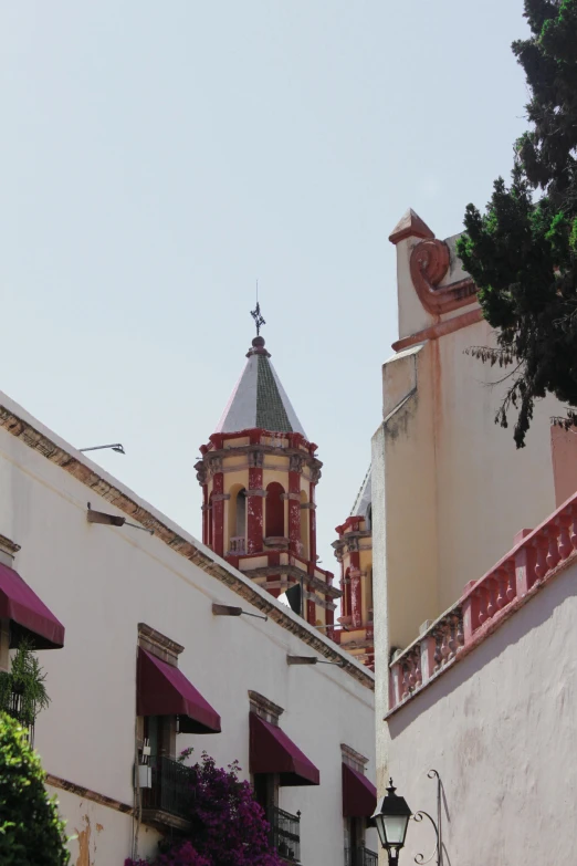 an old church steeple stands next to an older building with purple flowers on the balcony