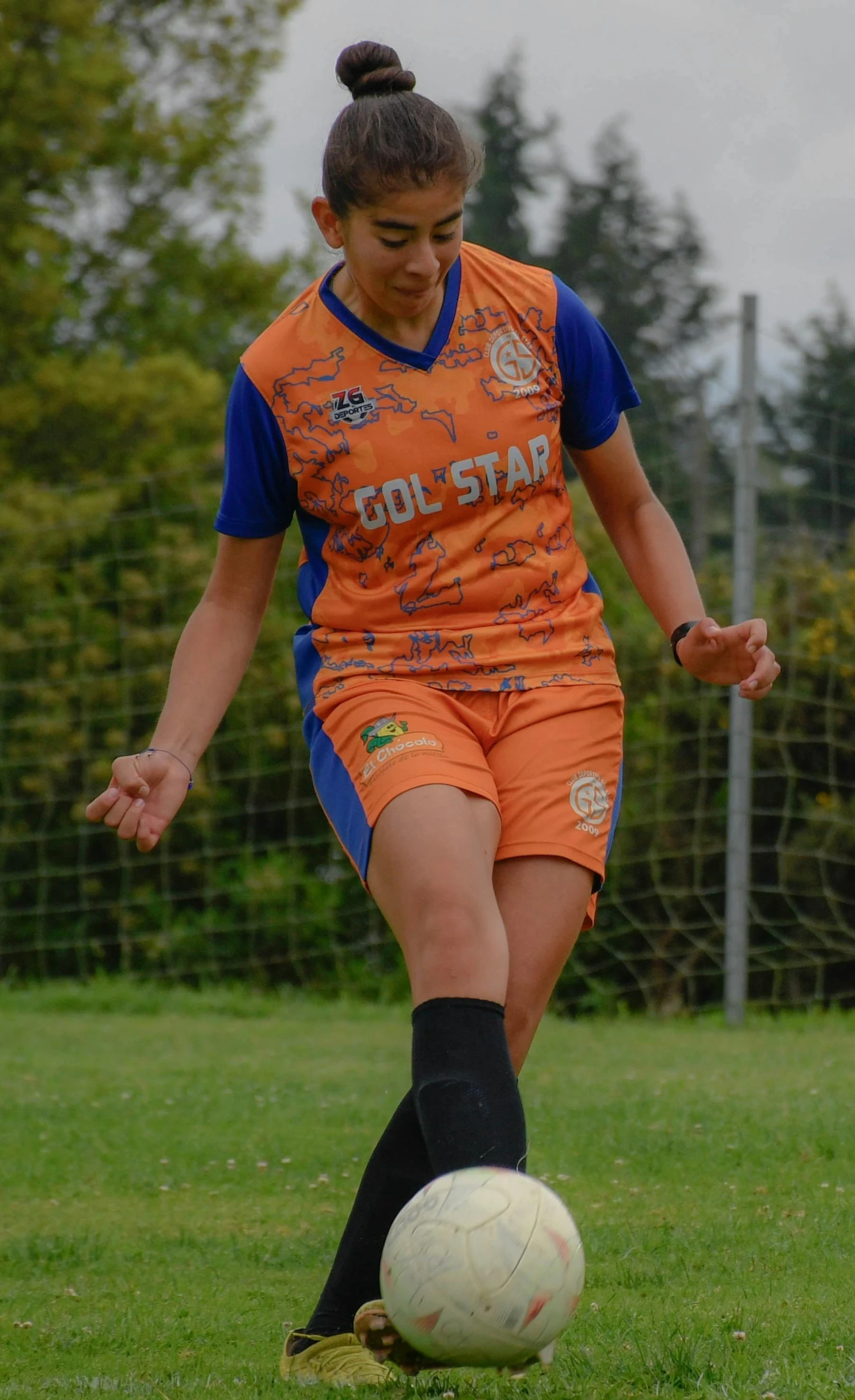 a girl wearing a soccer uniform is kicking a ball