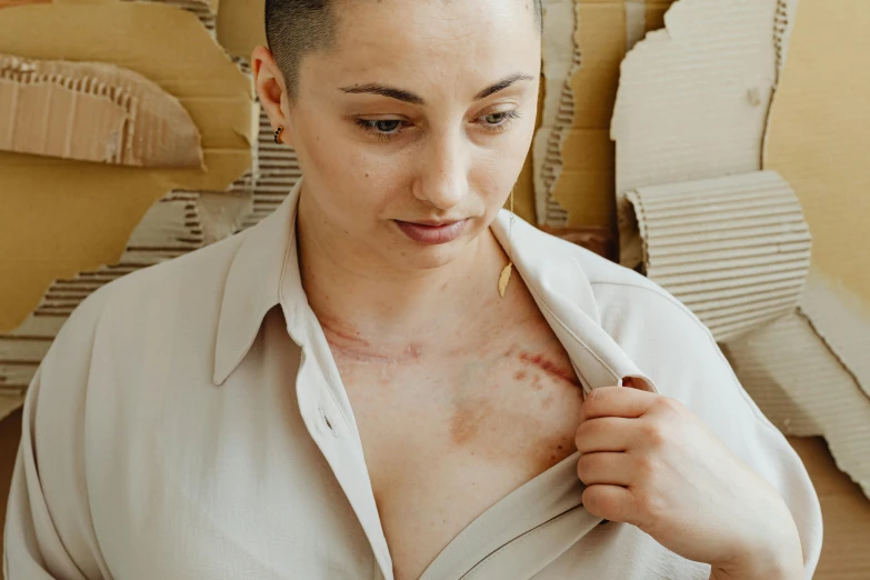 a woman putting on a blouse as she is in front of a pile of clothes