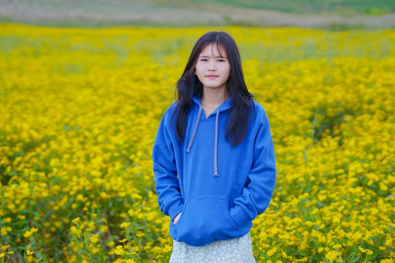 a girl in a blue sweatshirt and skirt stands in front of a field