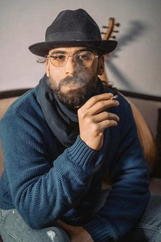 man in a blue sweater, hat and scarf holding a cigar