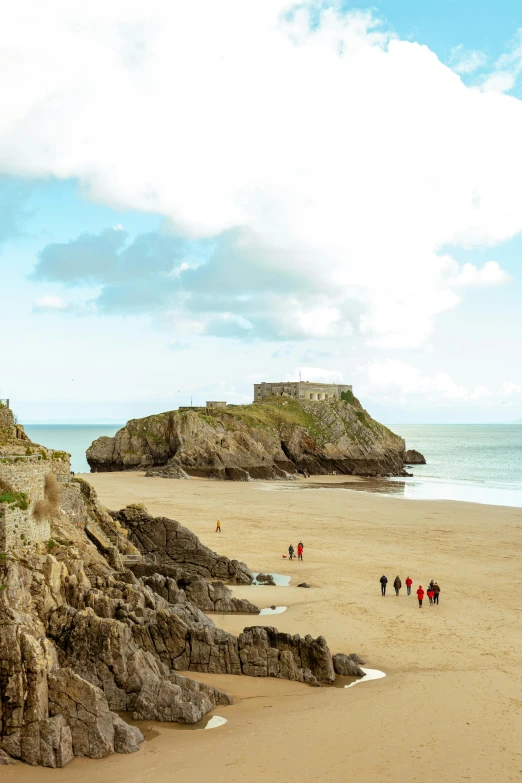 some people are walking along the beach under a cloudy sky