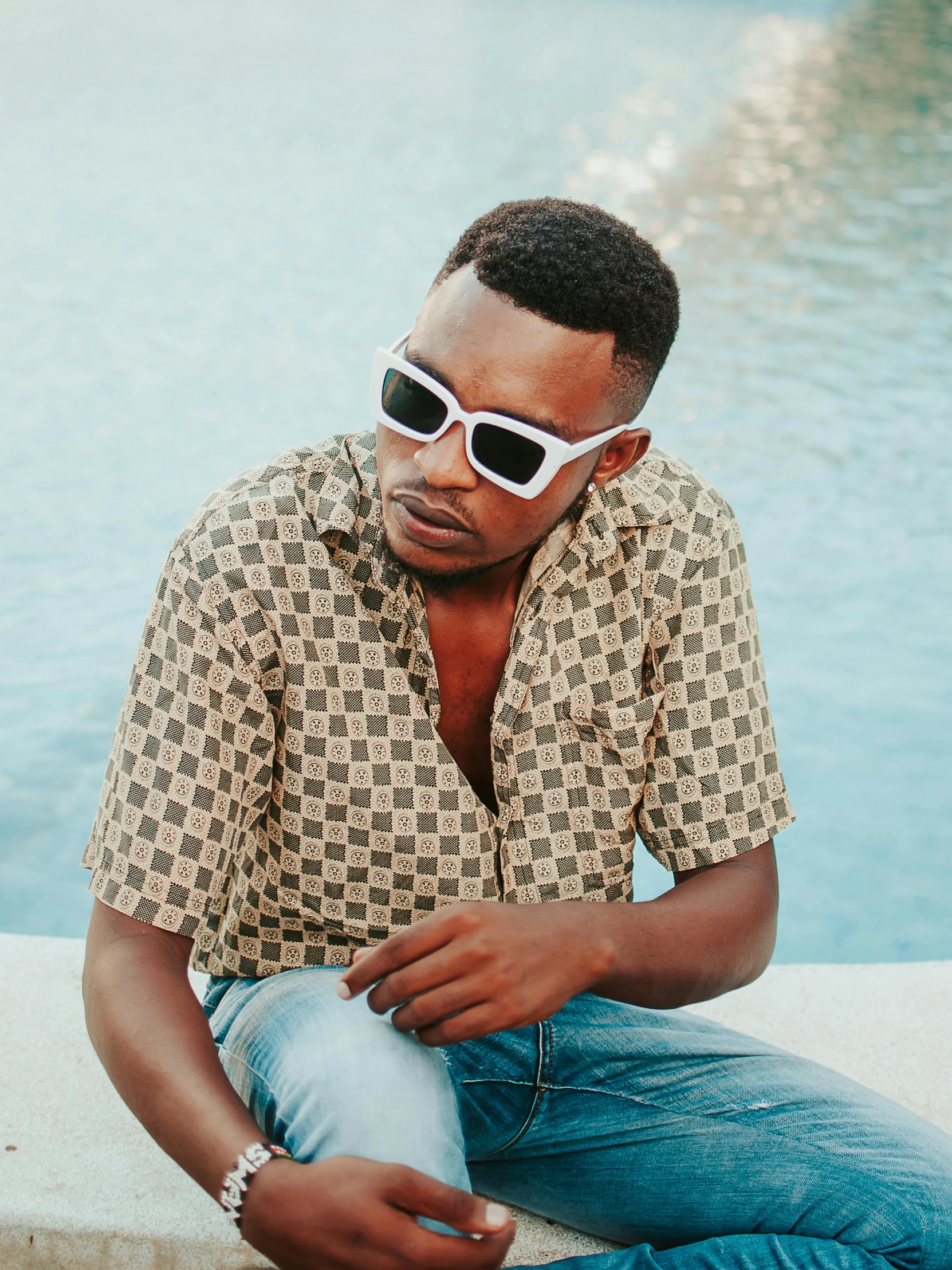 a man sitting next to a swimming pool wearing sunglasses