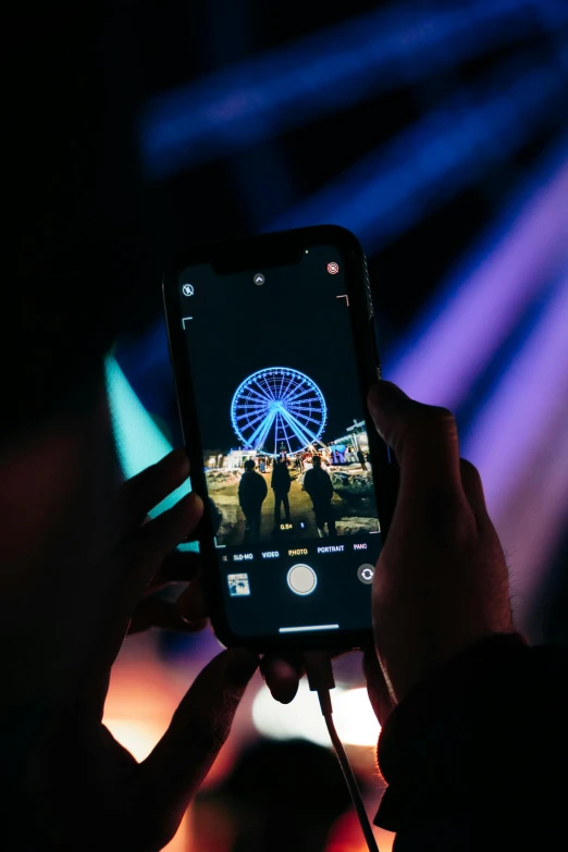 someone is holding a cell phone that is recording the movie of a ferris wheel