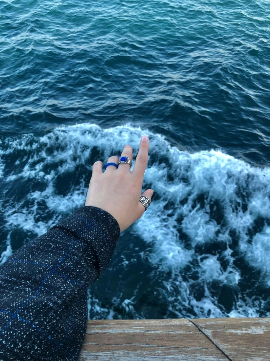 a person's hand with three stacked rings on their fingers by the ocean