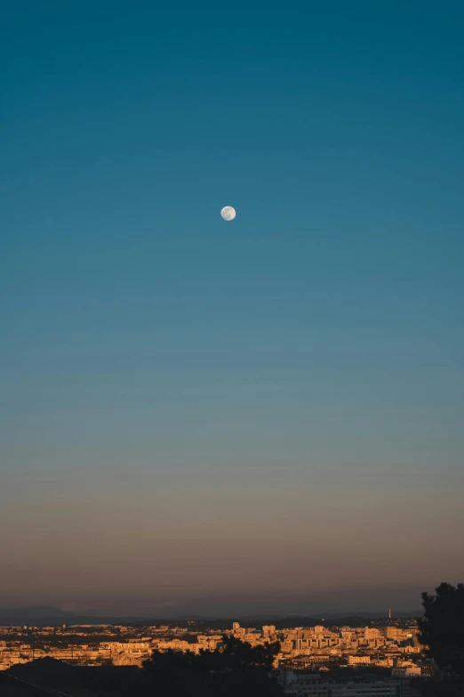 the moon is above a city with lights and buildings