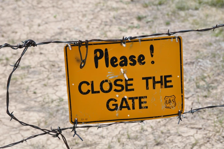 a sign hanging on a barbwire fence stating a close the gate