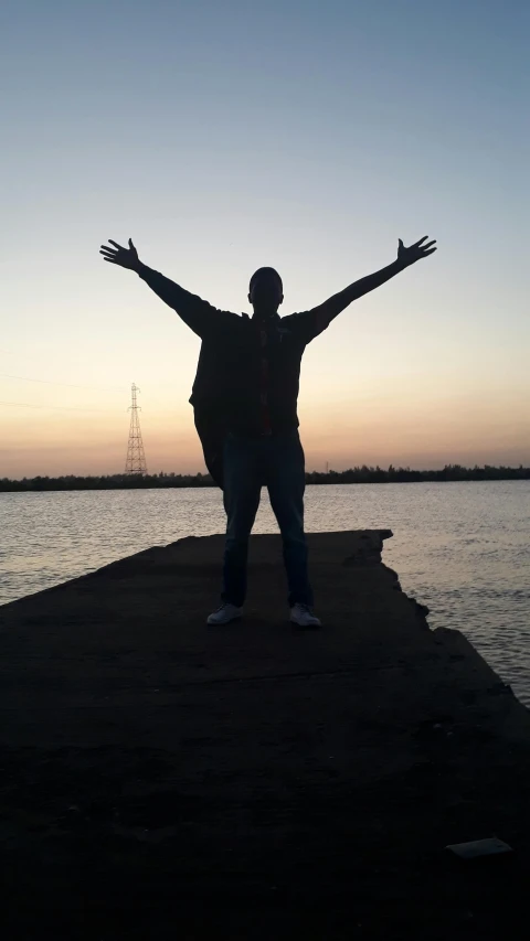 silhouette of man on rocks at edge of lake with arms outstretched