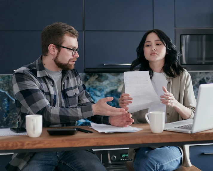 man and woman at a table reading papers and laptop computer