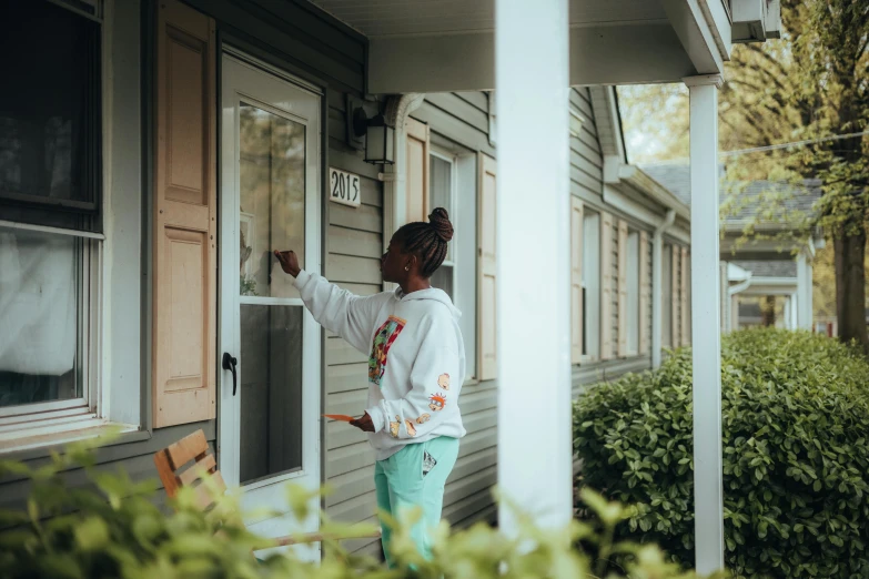 a girl in white shirt and green pants opening the door to a home