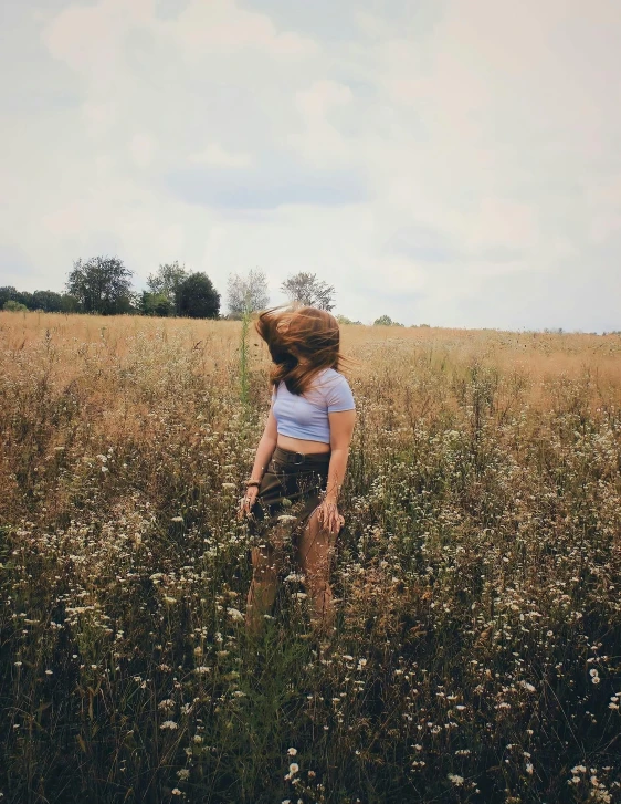 girl standing in grassy field with flowers near her