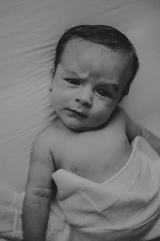 baby wrapped in white towel standing with folded head