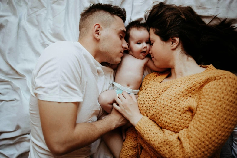 a man laying down on top of a woman holding a baby