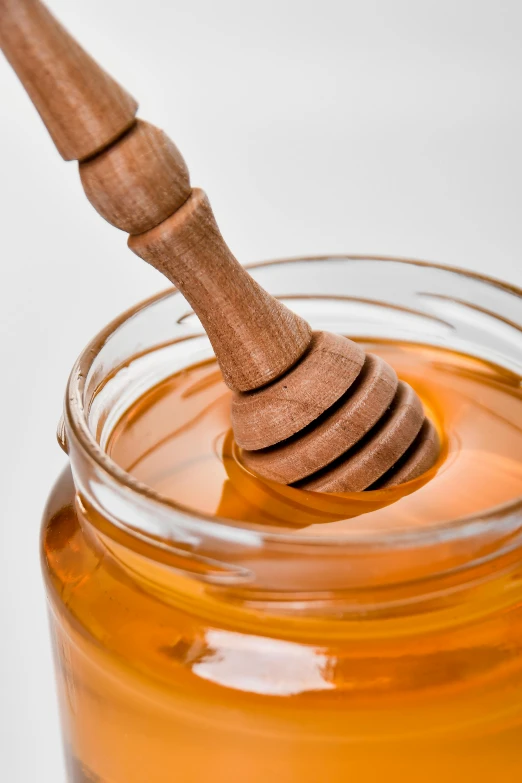 a wooden honey dipper and a glass jar filled with honey