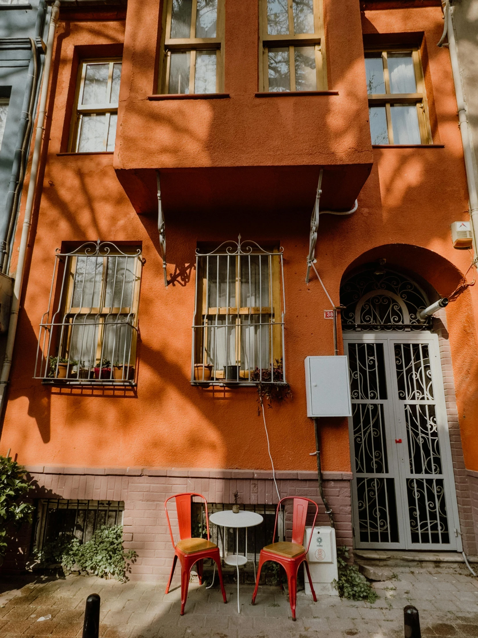 two red chairs next to a round table outside of a orange building