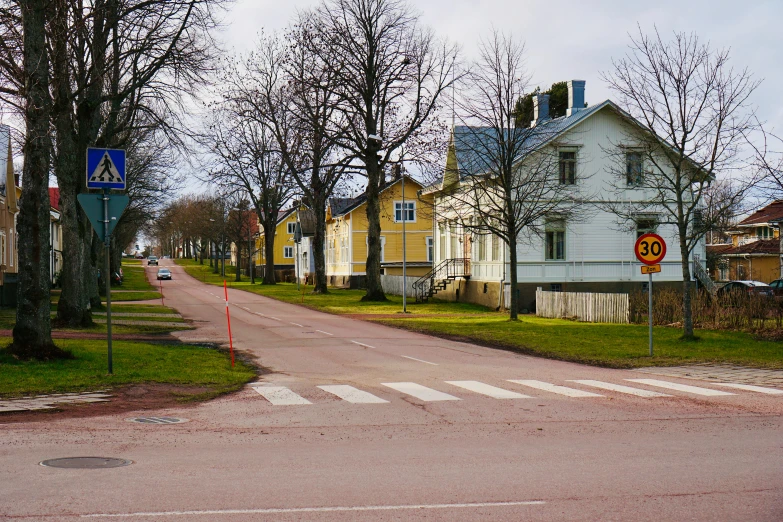 several old houses are lining the street as a yellow crosswalk is painted