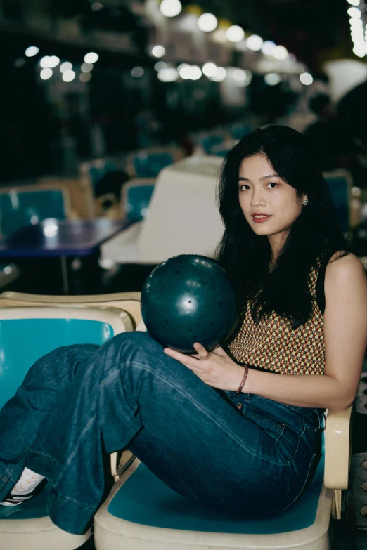 a woman holding a bowling ball and sitting in a chair