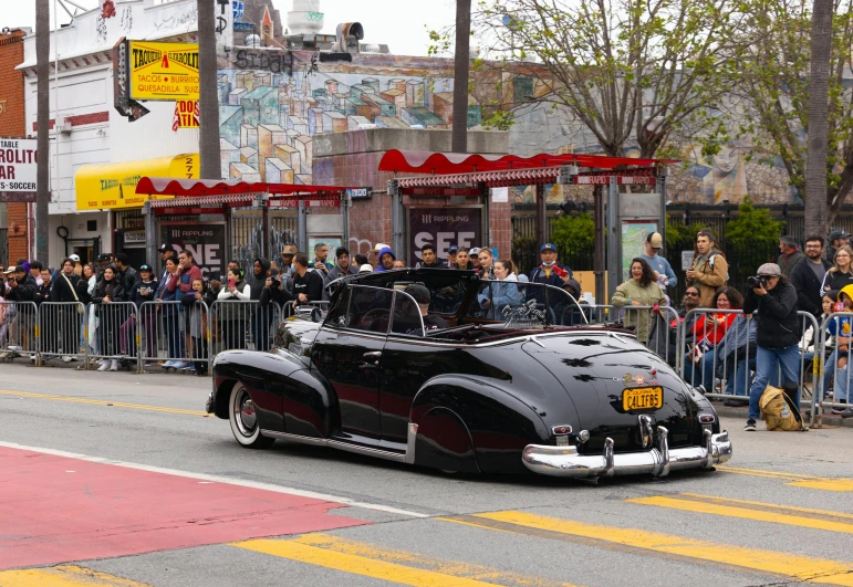 vintage vehicle driving down the street as a crowd watches