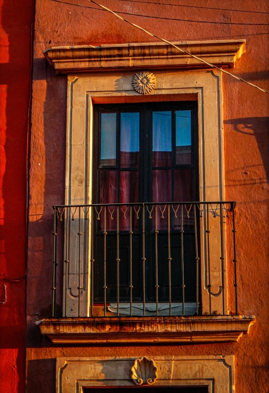 a brown building with a iron balcony, a window and sign on the front