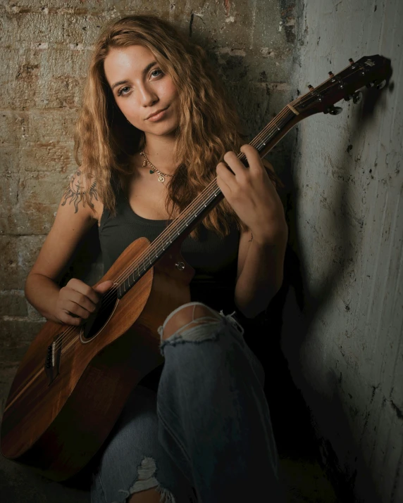 a person sitting and playing a guitar in front of a wall