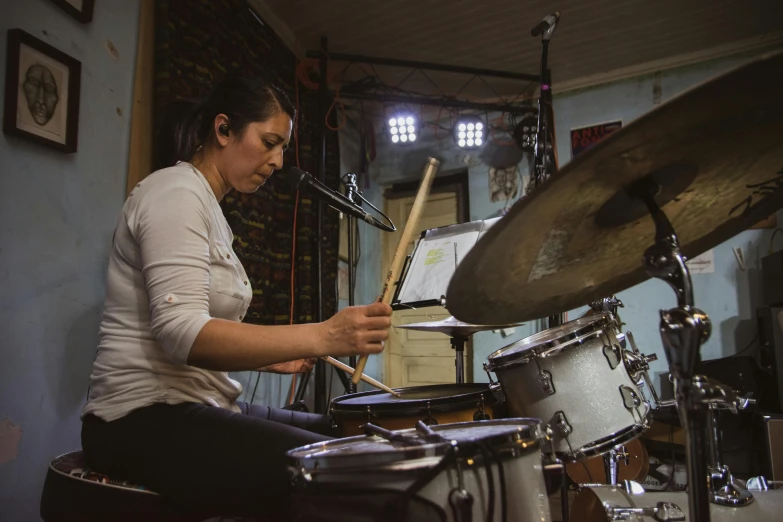 a woman holding drums near her face as she sits on the floor